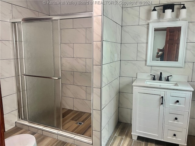 bathroom featuring a shower with shower door, tile walls, vanity, and toilet