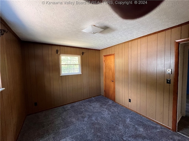 spare room featuring a textured ceiling, wooden walls, and carpet flooring