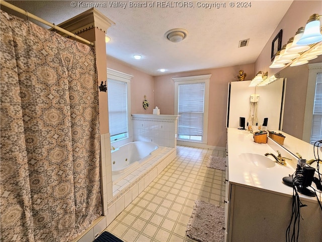 bathroom with a textured ceiling, tiled tub, vanity, and tile patterned floors