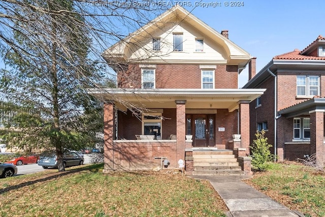 american foursquare style home with a chimney, brick siding, covered porch, and a front yard