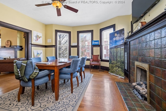 dining area with a fireplace, ceiling fan, and wood-type flooring