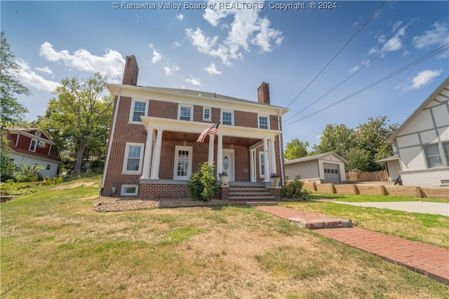 colonial inspired home with an outbuilding, a front yard, a garage, and covered porch