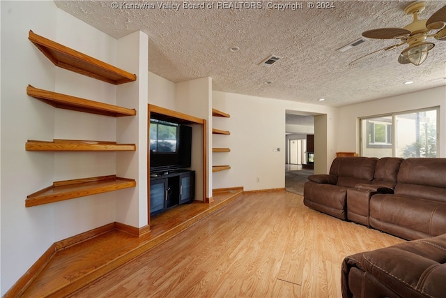 living room featuring ceiling fan, light hardwood / wood-style flooring, and a textured ceiling