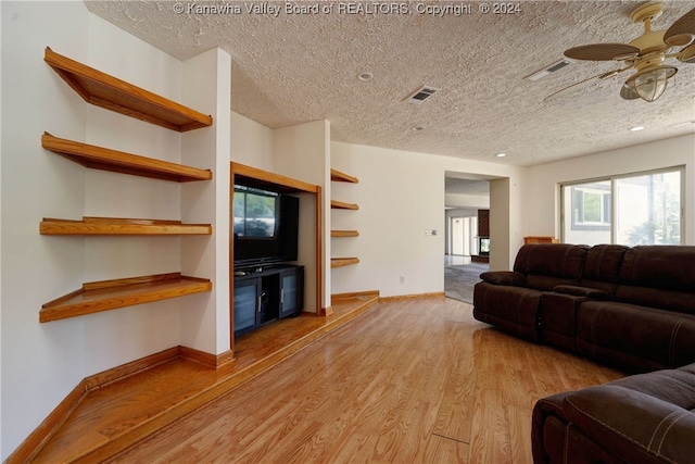 living room featuring light wood-type flooring, a textured ceiling, and ceiling fan