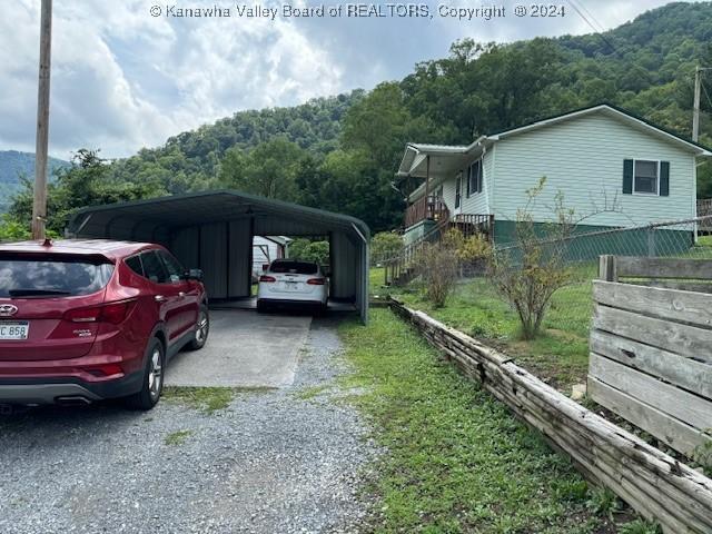 view of parking with gravel driveway, a carport, and a forest view