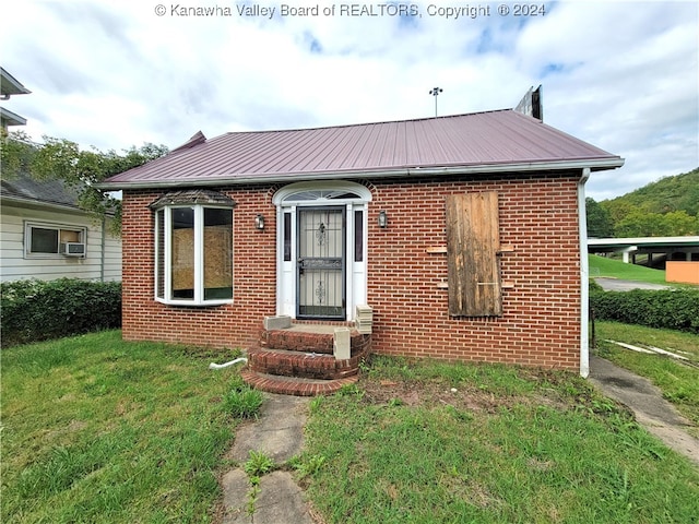 bungalow-style home featuring entry steps, metal roof, brick siding, and a front yard