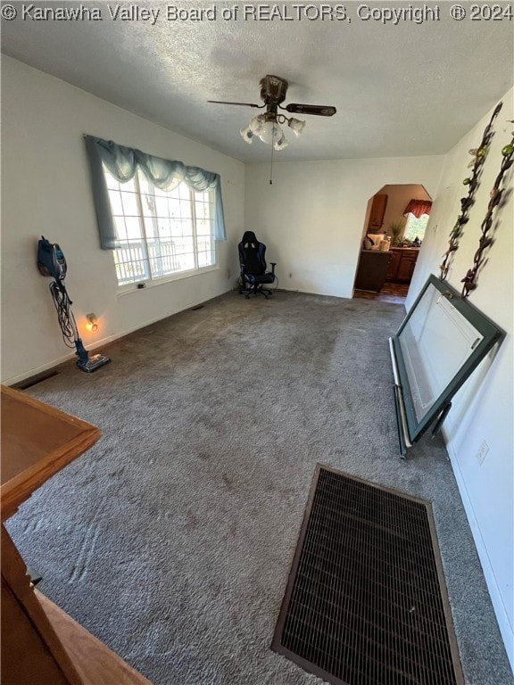 unfurnished living room with a textured ceiling, ceiling fan, and carpet flooring