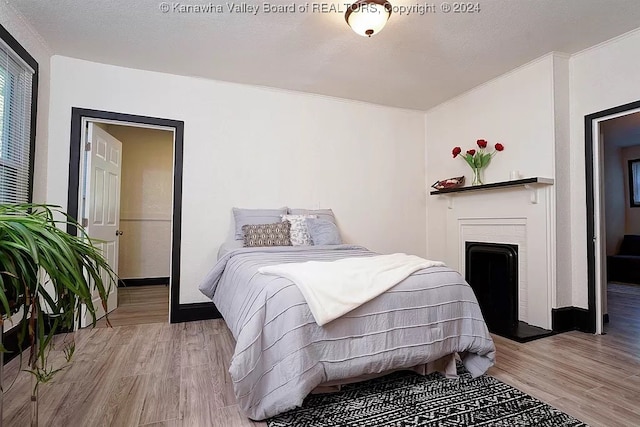 bedroom featuring a textured ceiling, a brick fireplace, and light hardwood / wood-style floors