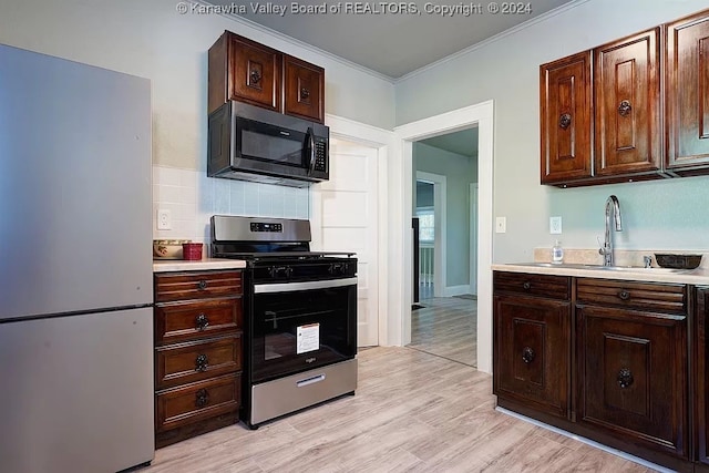 kitchen featuring appliances with stainless steel finishes, ornamental molding, light hardwood / wood-style floors, and sink