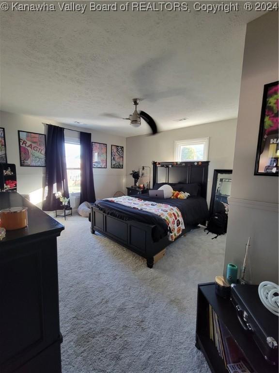 carpeted bedroom featuring multiple windows, ceiling fan, and a textured ceiling