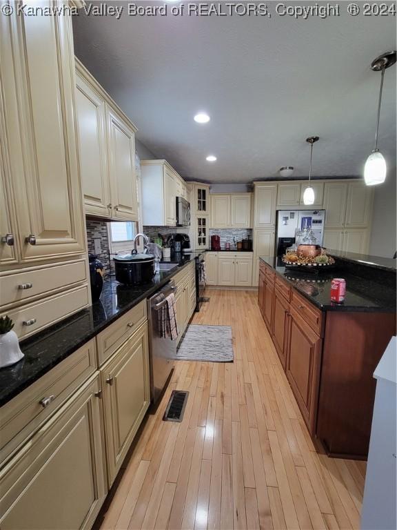 kitchen with decorative light fixtures, appliances with stainless steel finishes, light hardwood / wood-style floors, decorative backsplash, and dark stone counters