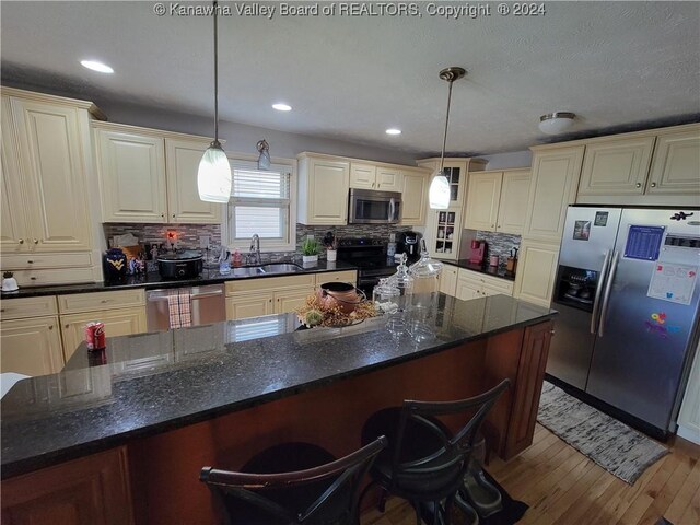 kitchen with a breakfast bar area, pendant lighting, cream cabinets, appliances with stainless steel finishes, and sink