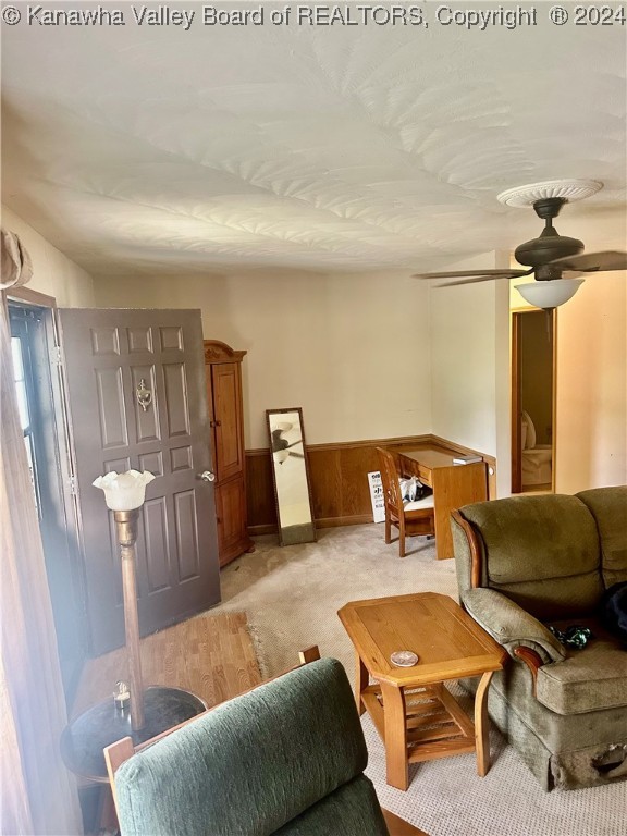 carpeted living room with ceiling fan and wooden walls