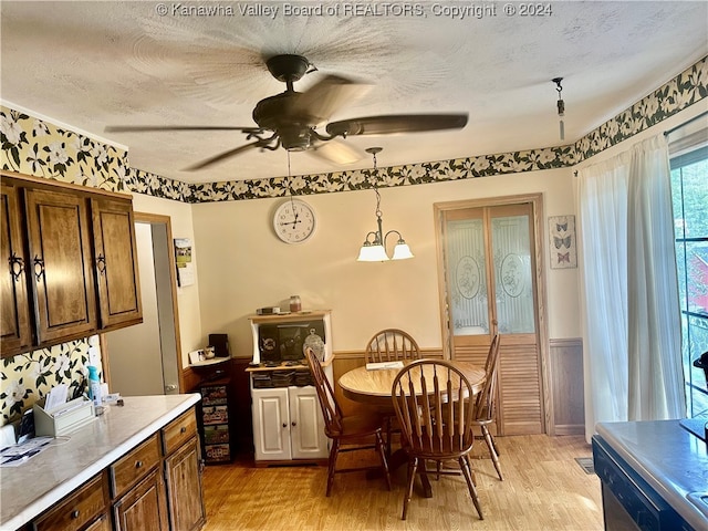 dining area with light wood-type flooring, ceiling fan with notable chandelier, wood walls, and a textured ceiling