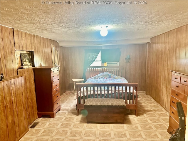 bedroom featuring light parquet floors, wood walls, and a textured ceiling