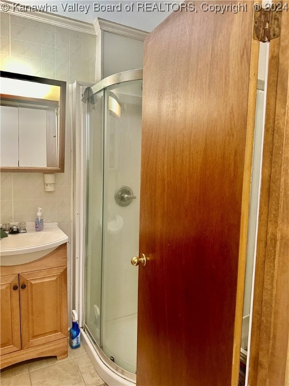 bathroom featuring tile patterned flooring, vanity, tasteful backsplash, tile walls, and a shower with shower door