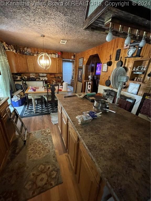 kitchen with a textured ceiling, wood walls, light hardwood / wood-style flooring, pendant lighting, and a chandelier