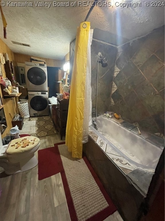 bathroom featuring a textured ceiling, shower / bath combination with curtain, stacked washer / drying machine, toilet, and hardwood / wood-style flooring