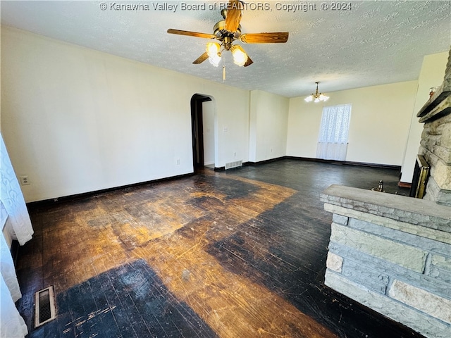 living room with ceiling fan with notable chandelier, a fireplace, a textured ceiling, and dark hardwood / wood-style flooring