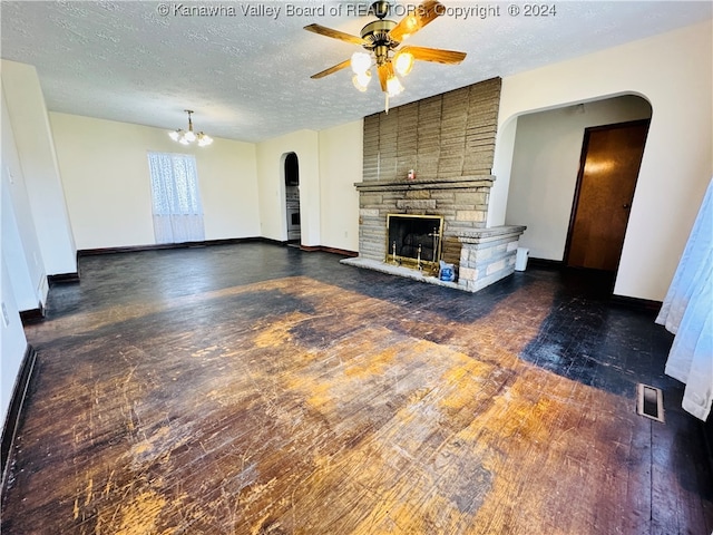 unfurnished living room with ceiling fan with notable chandelier, a textured ceiling, dark hardwood / wood-style flooring, and a stone fireplace