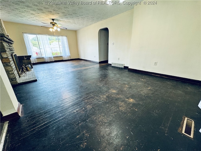 unfurnished living room featuring ceiling fan, a fireplace, dark hardwood / wood-style floors, and a textured ceiling