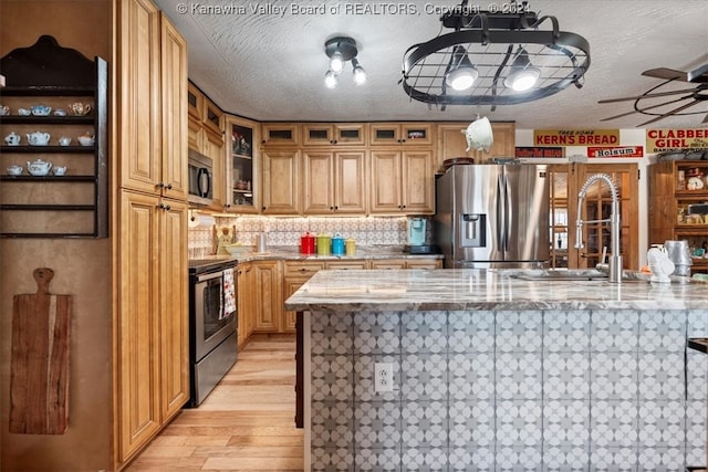 kitchen featuring light wood-type flooring, light stone counters, sink, ceiling fan, and appliances with stainless steel finishes