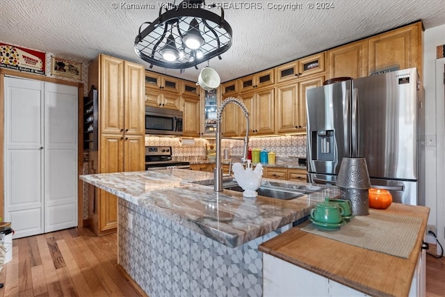 kitchen with an island with sink, backsplash, appliances with stainless steel finishes, and light hardwood / wood-style floors