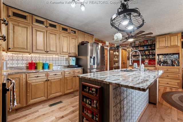 kitchen with ceiling fan, stainless steel fridge with ice dispenser, a kitchen island with sink, and light hardwood / wood-style flooring