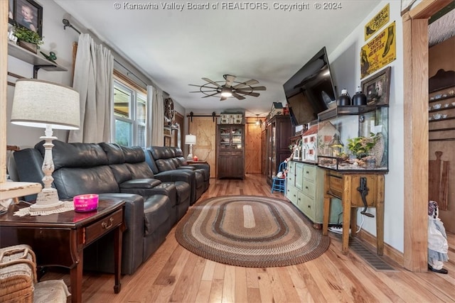 living room featuring a barn door, ceiling fan, and light hardwood / wood-style flooring