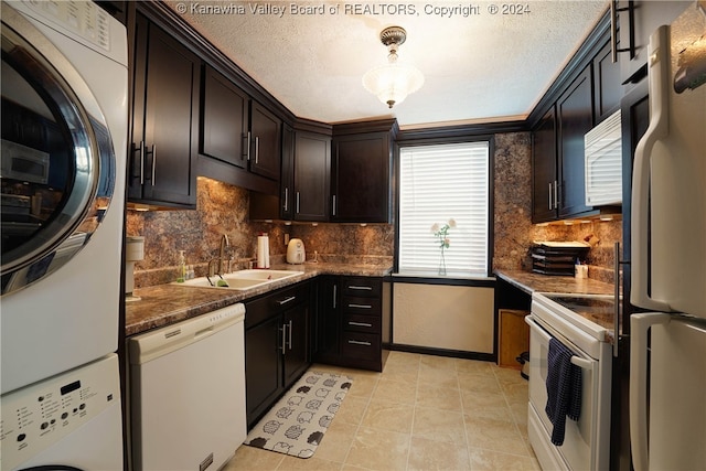 kitchen featuring light tile patterned floors, white appliances, stacked washing maching and dryer, sink, and a textured ceiling