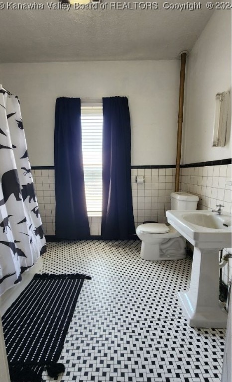 bathroom with a textured ceiling, tile walls, toilet, and a shower with curtain