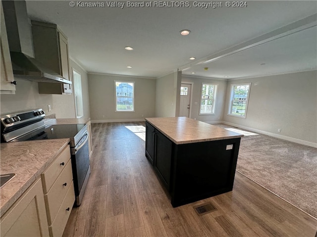 kitchen with wall chimney exhaust hood, crown molding, a center island, electric range, and hardwood / wood-style flooring