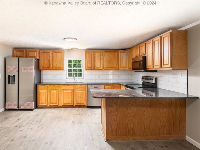 kitchen featuring light wood-type flooring, tasteful backsplash, kitchen peninsula, and stainless steel appliances