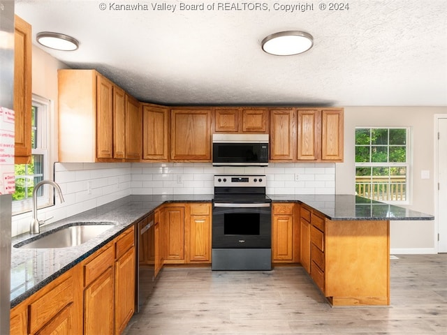 kitchen featuring stainless steel appliances, sink, kitchen peninsula, dark stone countertops, and light wood-type flooring