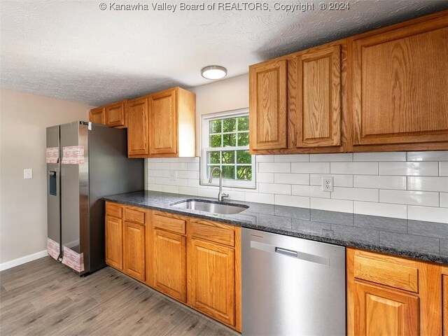 kitchen featuring a textured ceiling, backsplash, sink, appliances with stainless steel finishes, and light hardwood / wood-style floors