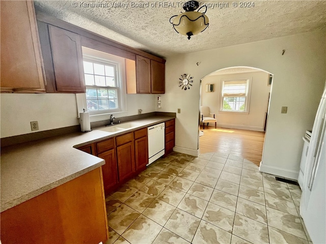 kitchen featuring light tile patterned floors, a textured ceiling, white dishwasher, and sink