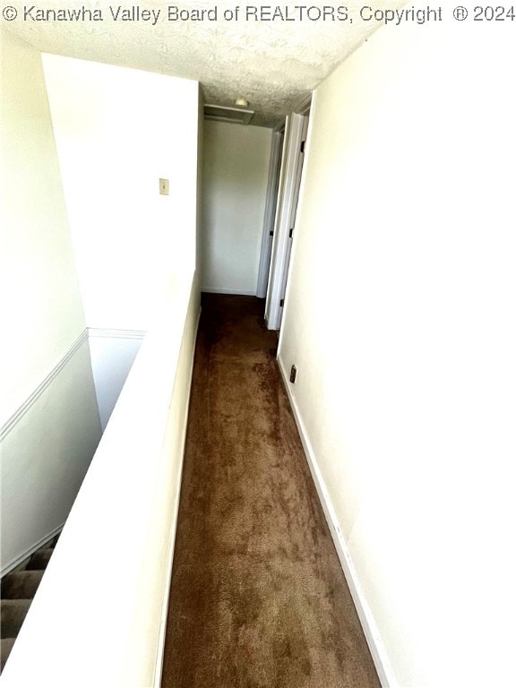 hall with dark colored carpet and a textured ceiling