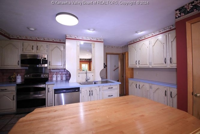 kitchen with tile patterned flooring, white cabinetry, tasteful backsplash, sink, and appliances with stainless steel finishes