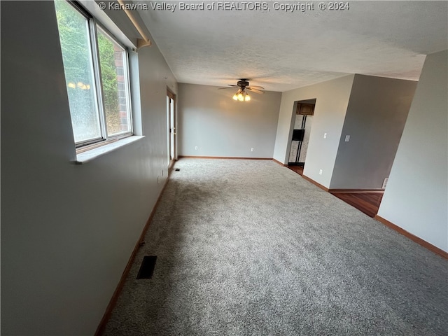 spare room featuring a textured ceiling, dark colored carpet, and ceiling fan