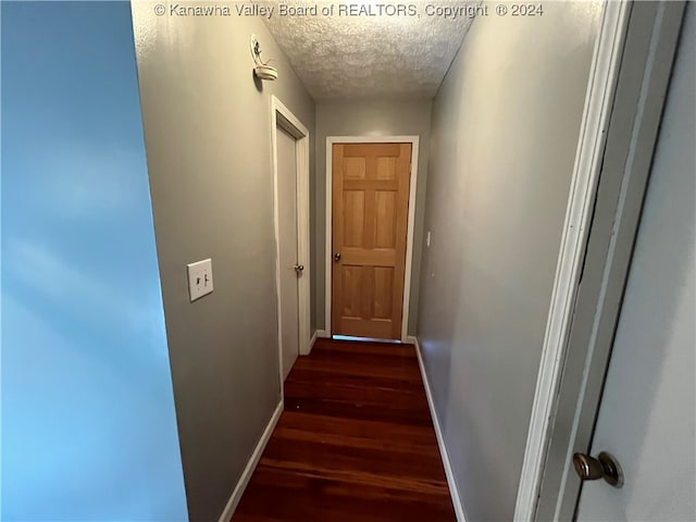 corridor with a textured ceiling and dark wood-type flooring