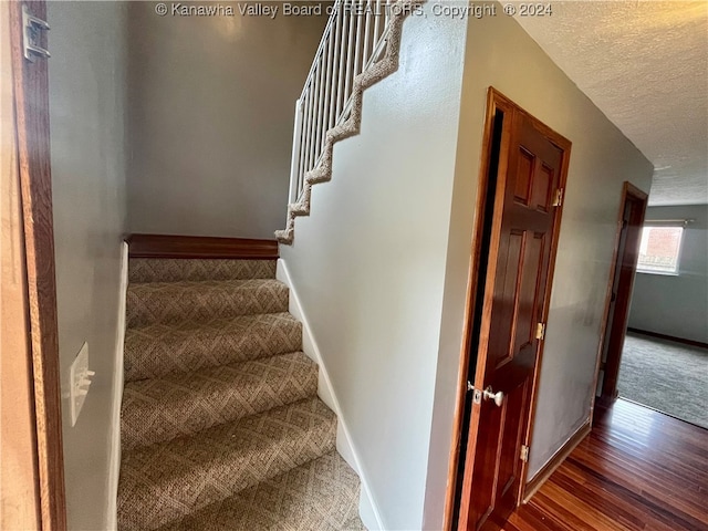 staircase featuring a textured ceiling and hardwood / wood-style floors