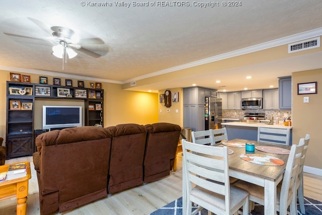 dining area featuring light wood-type flooring, a textured ceiling, ornamental molding, and ceiling fan