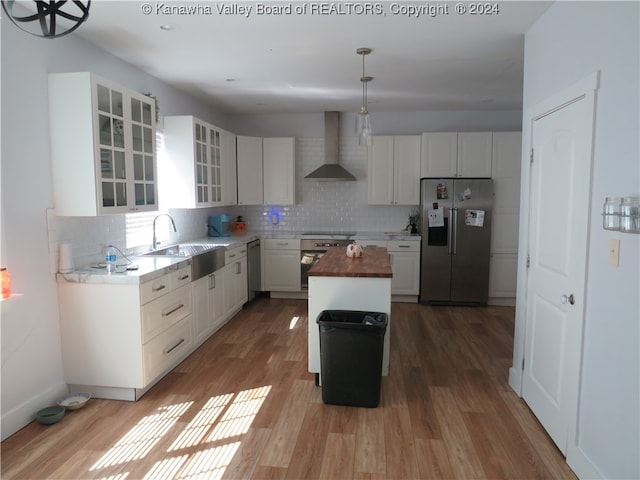 kitchen with a center island, sink, white cabinets, wall chimney range hood, and appliances with stainless steel finishes