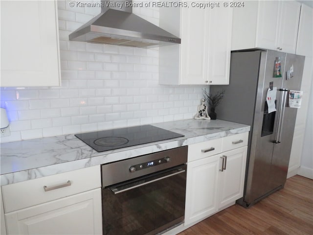 kitchen featuring white cabinets, tasteful backsplash, wall chimney exhaust hood, appliances with stainless steel finishes, and hardwood / wood-style floors