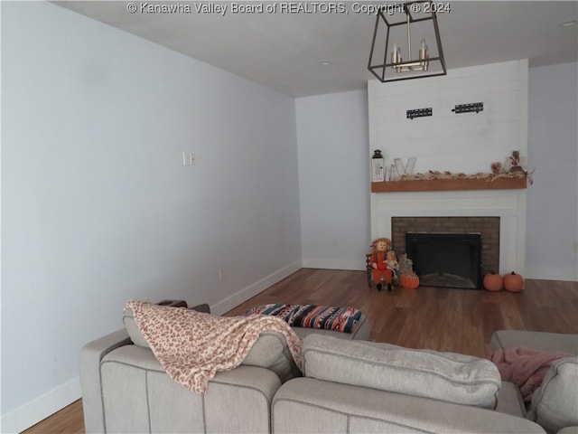 living room featuring a brick fireplace, a chandelier, and wood-type flooring