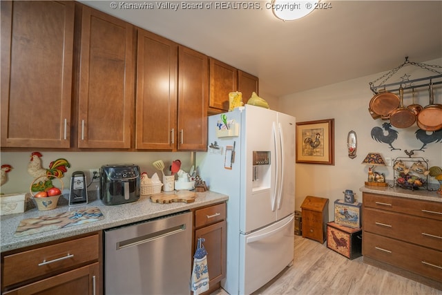 kitchen with light wood-type flooring, light stone countertops, dishwasher, and white refrigerator with ice dispenser