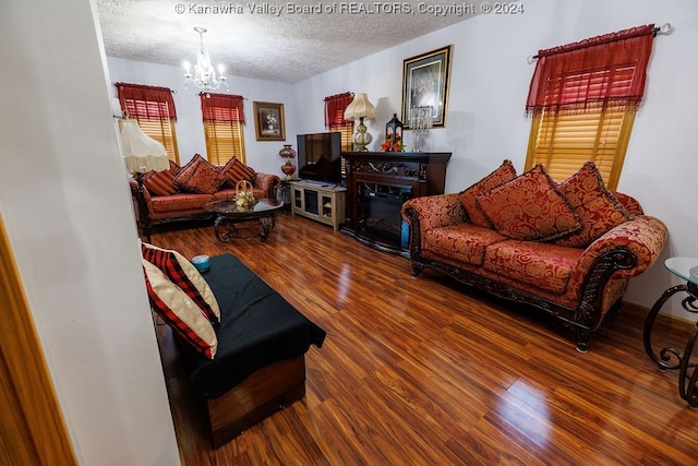 living room featuring wood-type flooring, a fireplace, a textured ceiling, and a notable chandelier