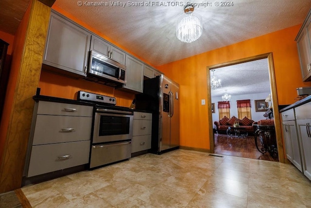 kitchen with appliances with stainless steel finishes, gray cabinets, a chandelier, and a textured ceiling