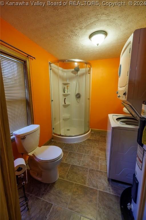 bathroom with stacked washing maching and dryer, toilet, a textured ceiling, and a shower with shower door