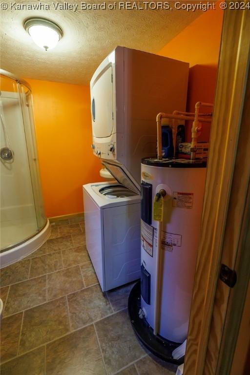 clothes washing area with stacked washer / drying machine, water heater, and a textured ceiling